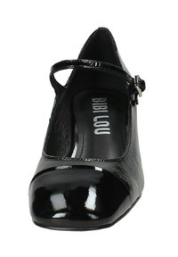 Scarpa in pelle verniciata nera con punta arrotondata, cinturino alla caviglia e corpo testurizzato. All'interno presenta una soletta con marchio.
