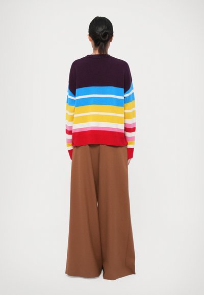 Maglione a maglia multicolore con strisce orizzontali in blu, giallo, rosso e rosa, abbinato a pantaloni larghi marroni. Texture morbida, vestibilità rilassata.