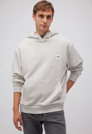 Light gray hoodie made of soft fabric, featuring a front pocket, adjustable drawstrings, and a small logo patch on the chest.