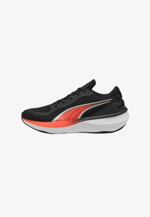 Chaussure de course noire avec une tige en mesh, accents rouges et argentés, semelle blanche rembourrée et semelle extérieure noire texturée. Présente des lacets traditionnels.