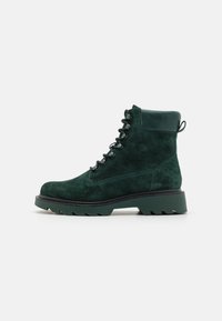 Bottes chevilles en suède vert avec une finition texturée, bout rond, laçage à l'avant et semelle épaisse avec un motif de semelle robuste.