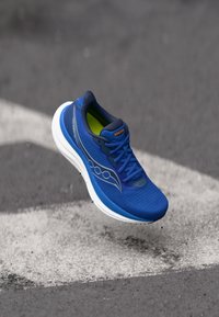 Blue running shoe with a mesh upper, padded collar, and white sole. Features pronounced branding and reflective accents on the side.