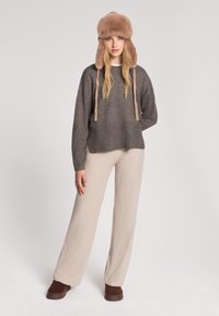 Szary sweter wełniany z ściągaczem, beżowe spodnie z ściągaczem oraz puszysta beżowa czapka z uszami. Całość dopełniają brązowe buty.