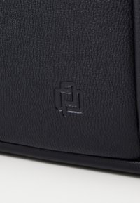 Surface en cuir texturé noir avec un petit logo carré entrelacé embossé près du bord inférieur.