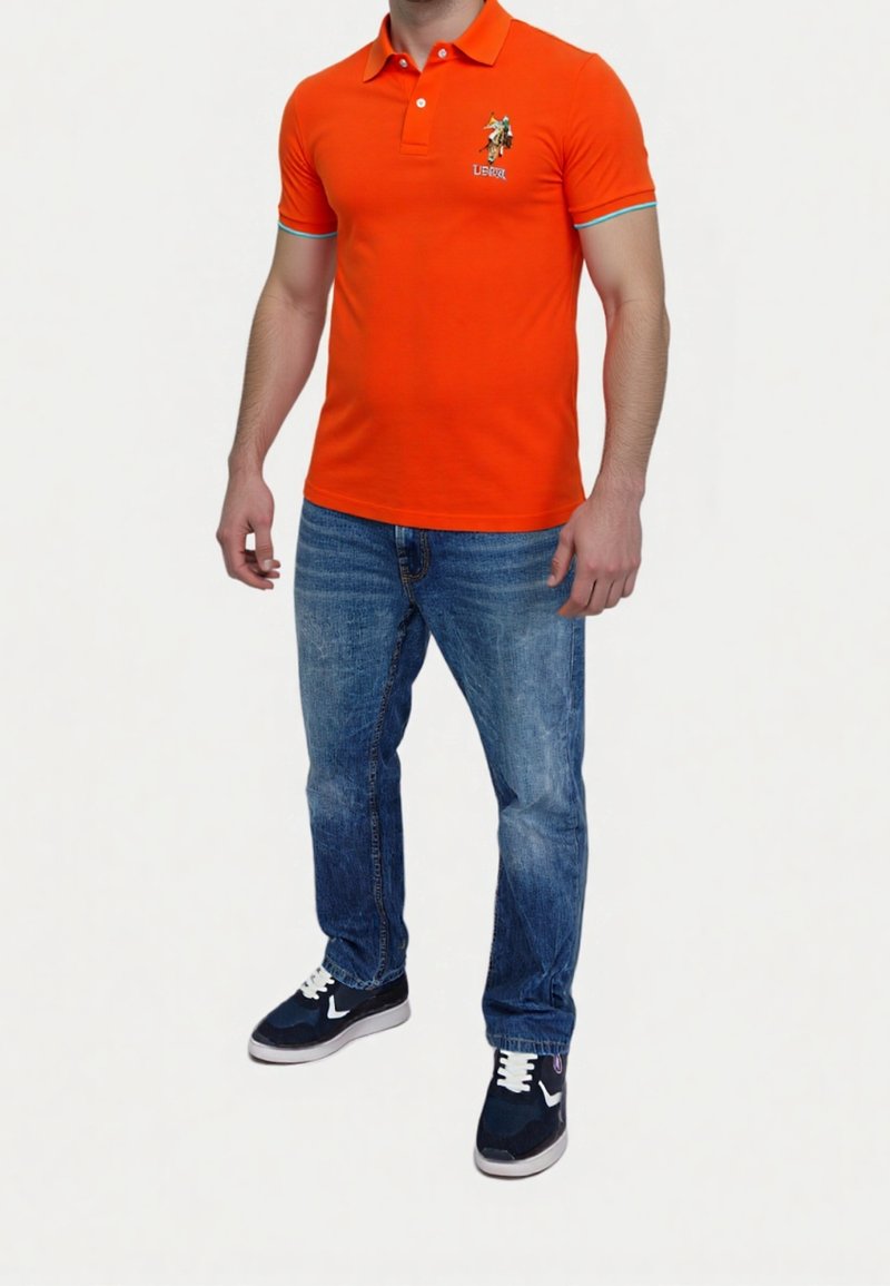 Orange polo skjorta med blå detaljer, broderad logotyp och en klassisk passform. I kombination med ljusblå denimjeans och mörka sneakers.
