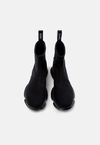 Botines negros de tela elástica, con una textura suave, puntera redondeada y suela de goma negra gruesa. Con tiradores en la parte posterior.