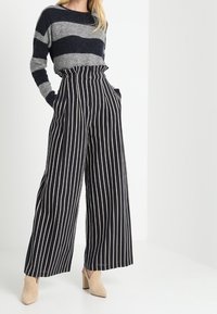 Stickad tröja med grå och marinblå ränder; högmidjade, vida byxor med vertikala svarta och beige ränder; parat med beige klackar.