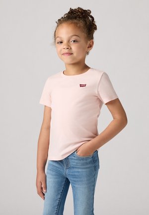 Camiseta de manga corta color rosa claro con cuello redondo y un pequeño parche del logo de Levi's en rojo oscuro en el pecho, combinada con jeans azules.