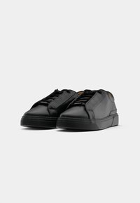 Pair of black low-top leather sneakers with laces, thick soles, and minimalist design on a plain white background.