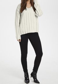 Knitted cream sweater with V-neck and vertical stripes, paired with black skinny jeans and shiny black ankle boots.
