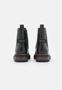 Botas Chelsea de cuero negro con paneles laterales elásticos, un tacón texturizado marrón y un logotipo de la marca en la parte trasera. Suela resistente con patrón de dibujo.