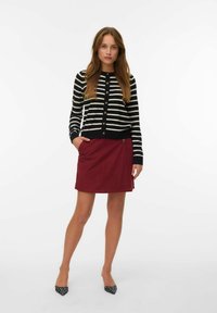 Cardigan rayé noir et blanc, boutonné, associé à une jupe drapée bordeaux avec une poche latérale et un détail de bouton. Talons à motifs noir et blanc.