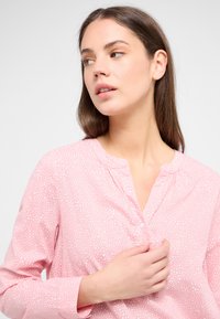 Rosa Hemdbluse mit weißem gepunktetem Muster, mit Kragen und langen Ärmeln. Hergestellt aus einem leichten, weichen Stoff.