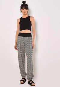 Černý krátký top kombinovaný s volnými kalhotami s vzorem v černobílé barvě, které mají elastický pas. Celý outfit doplňují černé sandály.