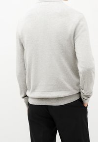Maglione grigio con una texture liscia, polsini e orlo a coste. Presenta una scollatura tonda e una vestibilità casual. Indossato sopra pantaloni scuri.
