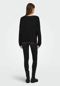 Pull noir surdimensionné avec des manches longues, un col large et une finition texturée, associé à un jean noir slim et des bottes noires épaisses.