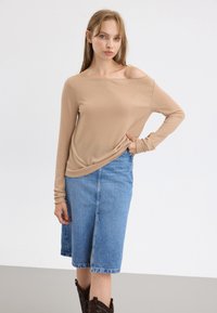 Beige ribbet langermet topp med av-shoulder design, parret med en lys blå denim midi-skjørt med splitt foran. Brune vestlige støvler.