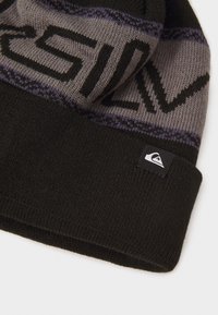 Berretto lavorato a maglia in nero con motivo grigio e viola, caratterizzato da audace lettering nero. Piccolo patch con logo sul bordo. Texture morbida.