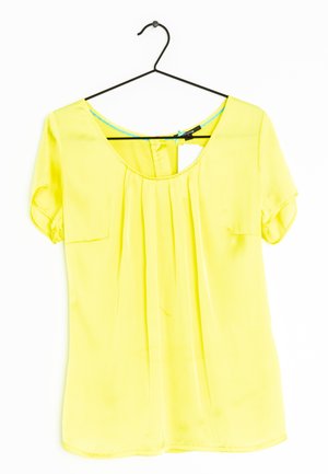 Blusa gialla a maniche corte su un appendiabiti nero, con una parte anteriore plissettata, scollo a barca e una piccola tasca sul petto. Tessuto liscio e leggero.