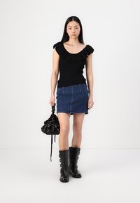 Svart ribbestrikket topp med volang hals, kombinert med et denimbunnkort skjørt. Svart knelengde støvler med spennende detaljer og en svart floral snøreveske.