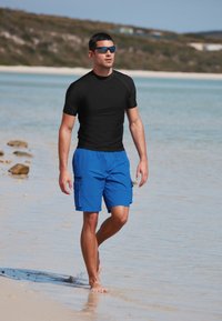 Schwarzes Rashguard mit kurzen Ärmeln, kombiniert mit blauen Cargo-Badeshorts mit Seitentaschen und einem leichten, schnell trocknenden Material.