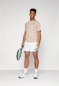 Beež lühikeste varrukatega sportlik särk sinise logoga, valged püksid, tennisepalli ja reketiga. Valged spordijalatsid siniste detalidega.