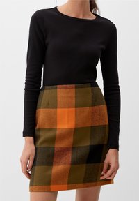 Zwarte lange mouwen top gecombineerd met een groen, oranje en zwart geruit wollen rok. De rok heeft een getailleerde pasvorm en een subtiele textuur.