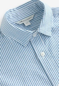 Plava i bijela prugasta pamučna košulja s okovratnikom na kopčanje, glatke teksture i s dva bijela dugmeta sprijeda.