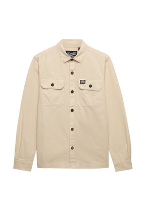 Chemise beige à manches longues avec col, deux poches à rabat sur la poitrine avec boutons, et une petite étiquette de marque au-dessus de la poche droite.