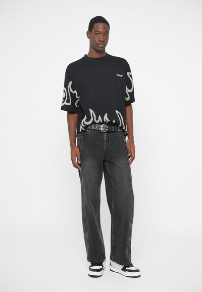 T-shirt noir avec motif de flammes blanches, associé à un jean droit taille haute foncé et des baskets noir et blanc.