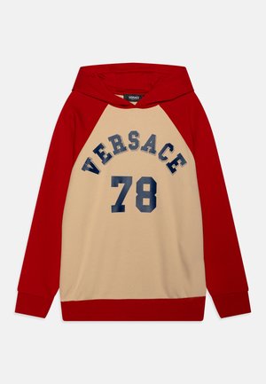 Mikina s kapucňou a červenými raglánovými rukávmi a béžovým telom. Na prednej strane sa nachádza tmavomodrý grafický text "VERSACE" a "78".
