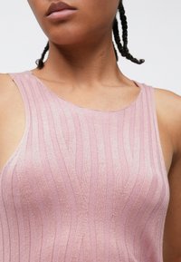 Ανοιχτόροζ αμάνικη μπλούζα με κάθετη ριμπ υφή, με στρογγυλεμένη λαιμόκοψη και λεία ύφασμα. Χωρίς εμφανή μεταλλικά εξαρτήματα ή σχέδια.