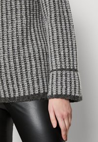 Grijs en zwart gestreepte gebreide trui met een gestructureerde weving, brede manchetten en zoomafwerking, gecombineerd met zwarte leren broek.
