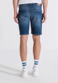 Bermuda in denim blu medio con orlo arrotolato, dotate di due tasche posteriori e un'etichetta in pelle al punto vita. Indossate con sneaker bianche e calze a righe.