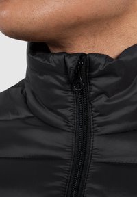 Giacca imbottita nera con colletto alto, dotata di zip frontale e texture trapuntata. Il materiale appare lucido, con dettagli di cucitura visibili.