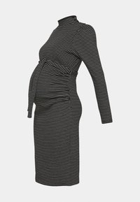 Robe de maternité à rayures horizontales noires et blanches avec manches longues, col montant et ceinture à nouer à la taille, vue de côté.