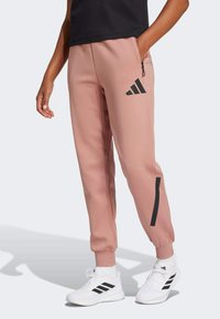 Rozā sporta bikses ar elastīgiem kāju galiem un sānu kabatu; ar melnu Adidas logo un akcenta svītrām uz kājām. Gluda, struktūrēta auduma.