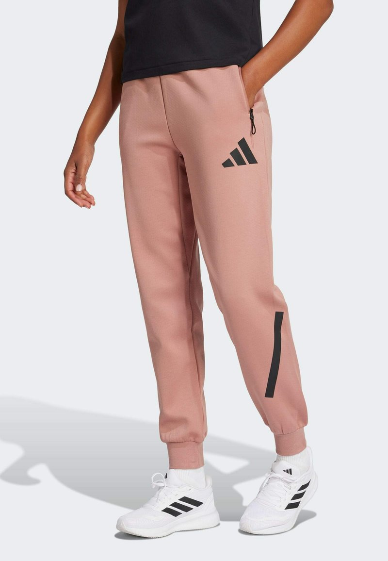 Rozā sporta bikses ar elastīgiem kāju galiem un sānu kabatu; ar melnu Adidas logo un akcenta svītrām uz kājām. Gluda, struktūrēta auduma.