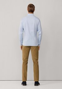 Camisa de botones en azul claro con mangas largas, combinada con pantalones de pana beige. La camisa tiene un cuello clásico y detalles de costura visibles.
