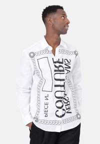 Witte overhemd met knopsluiting, versierd met zwart grafisch tekst en kettingpatronen. Lange mouwen met manchetten en een relaxte pasvorm.