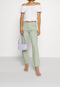 Blusa blanca sin mangas con patrón de ojal, combinada con pantalones de campana verde claro y un bolso de mano en relieve de color lavanda. Sandalias transparentes.