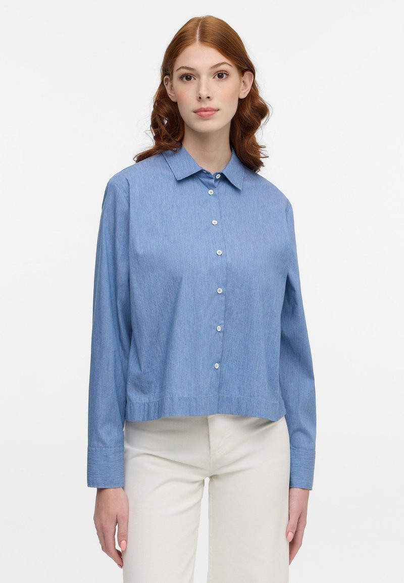Light blue button-up shirt made of soft fabric, featuring a collar, long sleeves, and a cropped hem. Buttons are white and round.