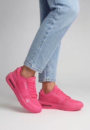 Person trägt hellblaue Jeans und knallpinke Sneakers mit sichtbaren Air-Sohlen vor neutralem Hintergrund.