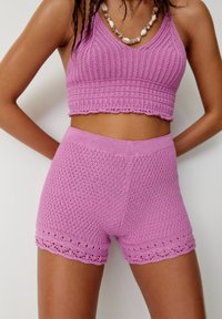 Różowy dzianinowy top w stylu crop z teksturowanym wzorem i koronkowym wykończeniem, w zestawie z dopasowanymi szortami o wysokim stanie, które mają podobne detale z koronkowego szydełka.