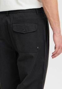 Pantalones negros de algodón con un ajuste relajado, que cuentan con un bolsillo trasero con cierre a botón y una pequeña etiqueta de logo en el lateral.