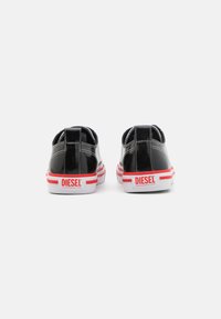 Sneaker basse in pelle verniciata nera con suole a strisce bianche e rosse a contrasto, con tacco brandizzato e design minimalista.