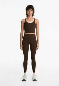 Dark brown activewear set featuring a crop top with a cream neckline and high-waisted leggings. Made of stretchy, textured fabric.