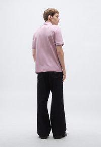 Lahek rožnat polo majica s kratkimi rokavi, kombinirana s širokimi temnimi hlačami. Minimalističen dizajn s kontrastnimi poudarki na ovratniku.