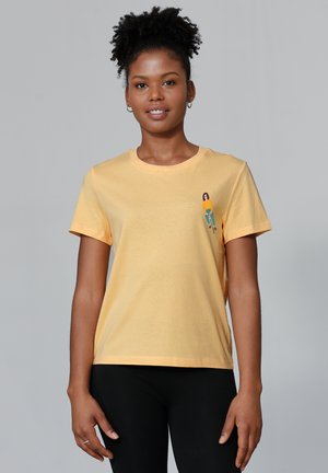 T-shirt en coton jaune à manches courtes, col rond, avec un petit motif graphique d'une silhouette sur la zone à gauche de la poitrine.