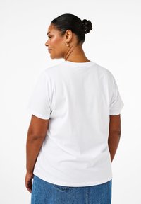 Camiseta de algodón blanca con un corte clásico, mangas cortas y cuello redondo, combinada con una falda de mezclilla. Sin patrones ni acentos visibles.